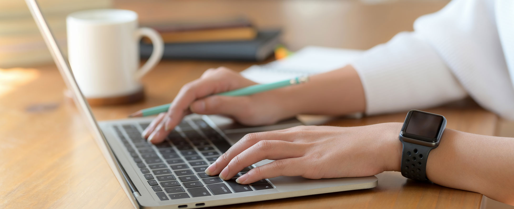 A person holds a pencil in their hand while typing on a laptop